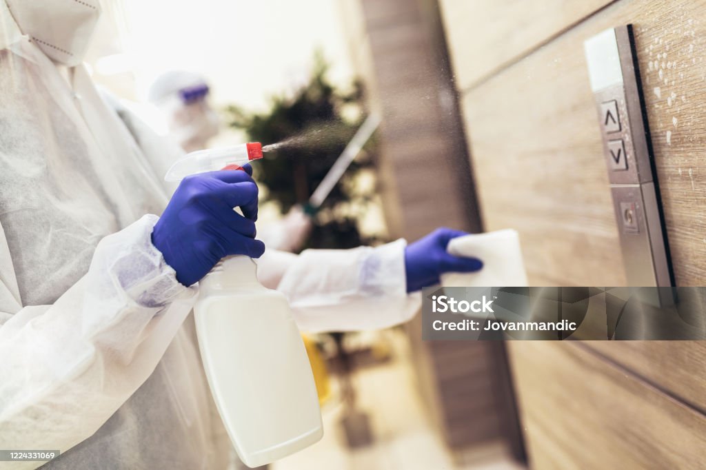 Staff using disinfectant from the bottle spraying an elevator push button control panel. Disinfection ,cleanliness and healthcare,Anti Corona virus (COVID-19). Disinfection Stock Photo