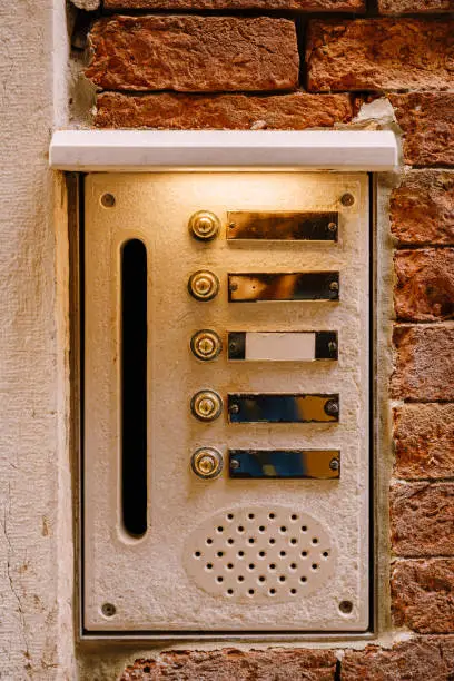 Photo of Close-ups of building facades in Venice, Italy. An old vintage intercom and a mailbox on a stone wall. On door where placed this old rusty doorbells.