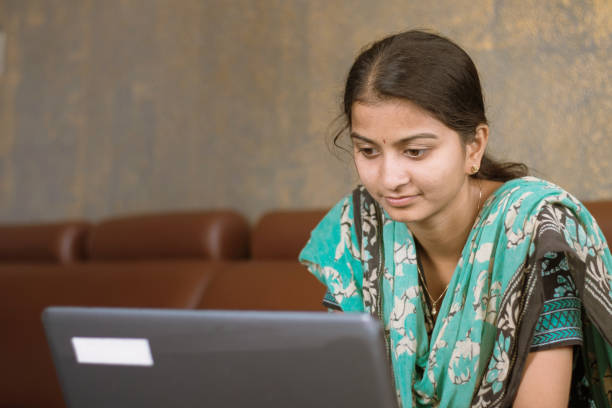 Smiling indian girl student or employee busy on laptop sit at home in casual dress, happy woman studying, e-learning, using online software or technology app for work, education concept Smiling indian girl student or employee busy on laptop sit at home in casual dress, happy woman studying, e-learning, using online software or technology app for work, education concept. india train stock pictures, royalty-free photos & images