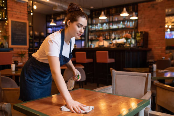 istock Pretty young waitress in apron using detergent and duster to clean table 1224342204
