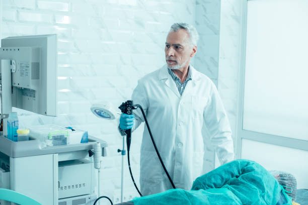 Medical worker and his patient before the endoscopy Serious mature doctor holding a modern endoscope and preparing for the procedure gastroenterology photos stock pictures, royalty-free photos & images