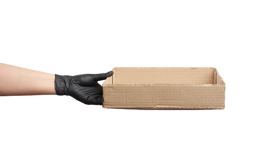 female hand in a black latex glove holds a brown cardboard box on a white background, safe and contactless delivery of on-line orders during epidemics