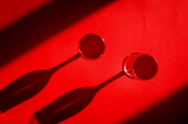 Two glasses of cocktail with red sparkling wine on red background in natural sunlight with shadows. Minimalist creative art composition. Conceptual image.  Simple visual concept.