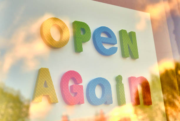 Open again sign behind a window, small business welcoming customers.
