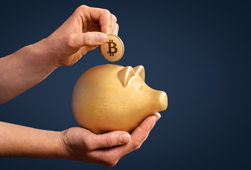 Woman inserting Bitcoin in gold piggy bank