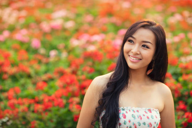 A woman looking sideways in front of a large number of geraniums.