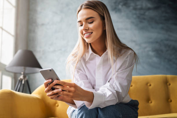 istock A beautiful woman works at home sitting on a yellow sofa, using a smartphone, writing messages, sharing photos 1224366353