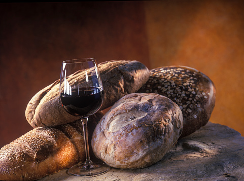 close up on various rustic Italian bread loafs and glass of red wine on stone underground