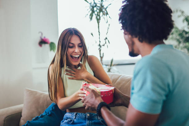 istock Smiling man surprises his girlfriend with present at home. 1224371025