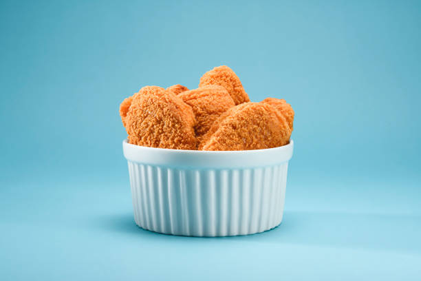 A portion of delicious and crispy chicken nuggets on a white ramekin A portion of delicious and crispy chicken nuggets on a white ramekin, on a teal or blue background. A popular fast food  made from chicken meat that is breaded or battered, then deep-fried or baked. Ideal to illustrate a restaurant or snack at home on a teal and orange theme. nugget photos stock pictures, royalty-free photos & images