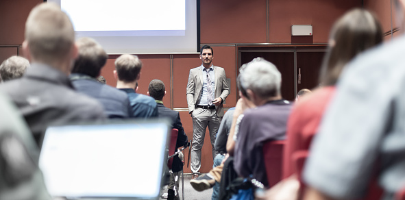 Image of large or medium group of people sitting in conference hall, and listening to public speaker, consultant, lecturer or professor, actively participating in the class by raising hands, clapping, voting or discussing. Image taken with Nikon D800 and 50 or 85mm lens, developed from RAW. Location: Europe