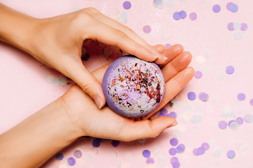 Flat lay composition with bath bombs in girls hand on pink background with festive confetti.