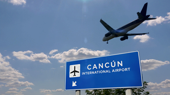 Airplane silhouette landing in Cancún, Mexico (Cancun). City arrival with international airport direction signboard and blue sky in background. Travel, trip and transport concept 3d illustration.