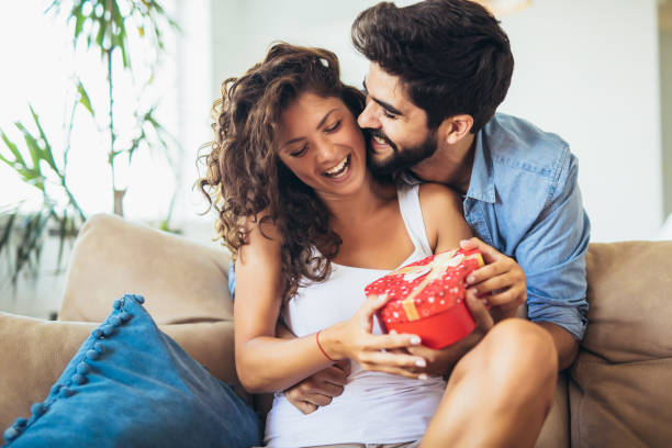 istock Smiling man surprises his girlfriend with present at home. 1224374114