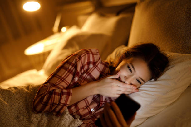 istock Beautiful young woman using mobile phone in bed at night 1224374755