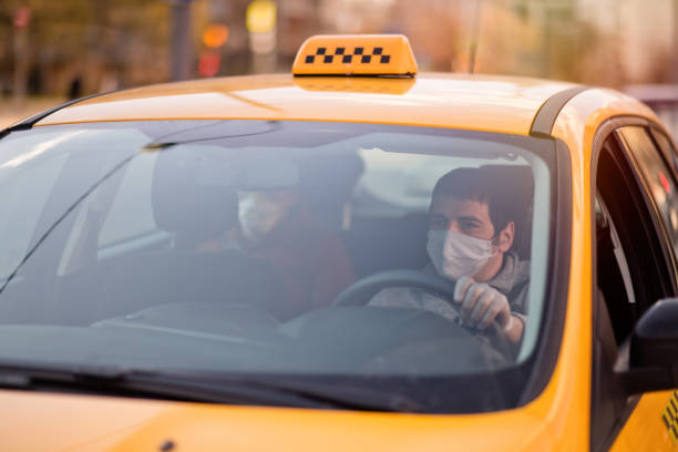 Taxi driver and his passenger are wearing protective masks during air pollution or illness epidemic Yellow taxi on a city street taxi driver photos stock pictures, royalty-free photos & images