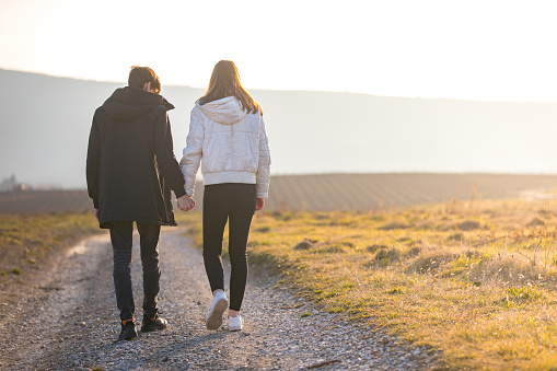 Rear View of Teenage Couple Walking on Dirt Road in Landscape With Meadows.