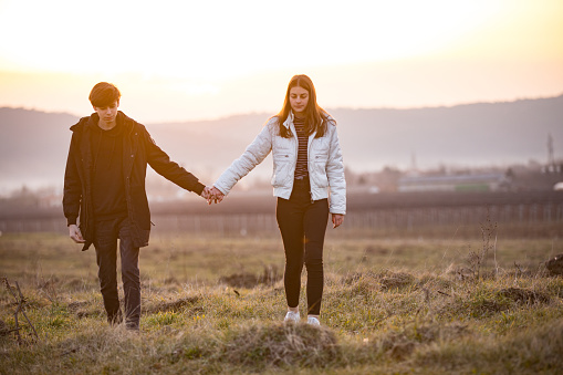 Front View of Teenage Couple Holding Hands and Walking on Meadow in Rural Scene.