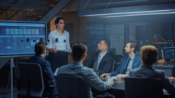 istock In the Corporate Meeting Room: Female Executive Talks and Uses Digital Interactive Whiteboard for Presentation to a Board of Directors, Investors. Screen Shows Growth Data. Late at Night Office 1224381278