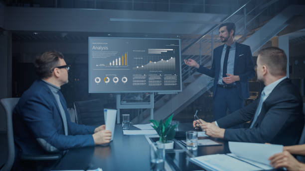 istock In the Corporate Meeting Room: Male Executive Talks and Uses Digital Interactive Whiteboard for Presentation to a Board of Directors, Investors. Screen Shows Growth Data. Late at Night Office 1224381332