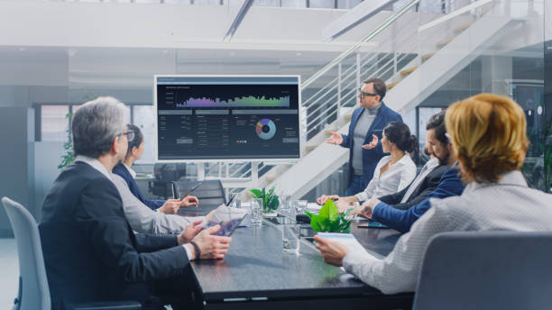 istock In Corporate Meeting Room: Creative Director Uses Digital Interactive Whiteboard for Presentation to a Board of Executives, Lawyers, Investors. Screen Shows Company Growth Data with Graphs 1224381342