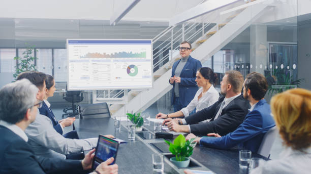 istock In Corporate Meeting Room: Creative Director Uses Digital Interactive Whiteboard for Presentation to Board of Executives, Lawyers, Investors, Businesspeople. Screen Shows Company Growth Data 1224381398
