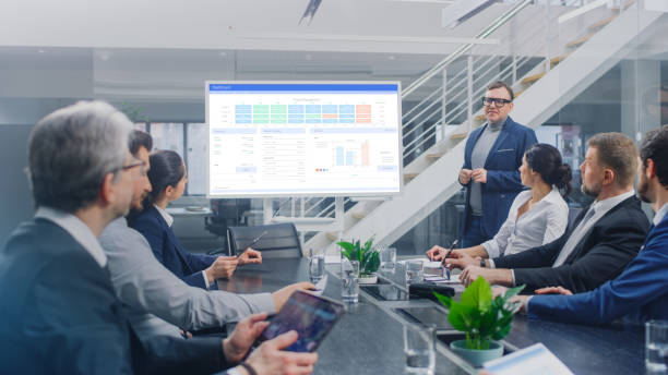 istock In Corporate Meeting Room: Creative Director Uses Digital Interactive Whiteboard for Presentation to a Board of Executives, Lawyers, Investors. Screen Shows Company Growth Data with Animated Graphs 1224381521