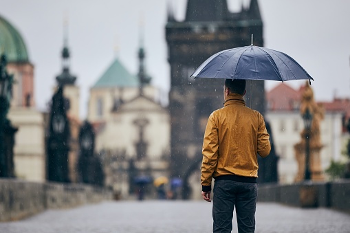 Lonely man with umbrella in heavy rain on empty Charles Bridge. Prague Czech Republic
