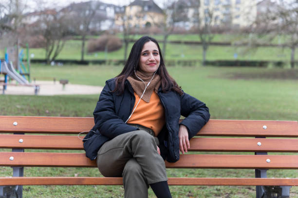 istock Young Woman Sitting on Bench with Head Turned Smiling at Camera 1224392915
