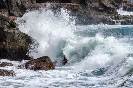 Large white waves of the sea break on the rocks. Breakwater near the small Village of Framura. La Spezia, Liguria, Italy, Europe. Mediterranean Sea.
