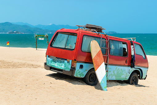 Old bus in the sand and surfboard on the beach