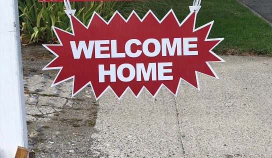 Welcome home sign hangs on a real estate for sale sign