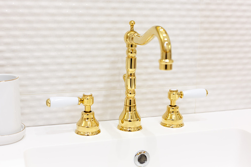 Bathroom faucet made of gold. Antique style. Gold-plated handles with white accents
