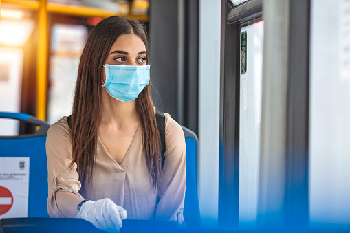 Woman wearing a sterile protective medical mask against coronavirus, Covid-2019 Asian pandemic sars virus while going in a public bus in a European city street looking ahead.