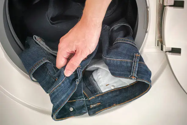 Photo of Man picking up jeans out of the washing machine