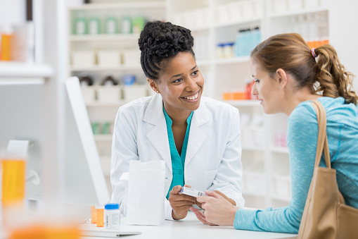 A confident mid adult African American pharmacist discusses a prescription medication's instructions and side effects with a female customer.