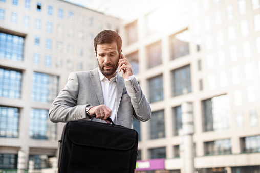 Mid adult businessman late to work checking time and talking on phone.