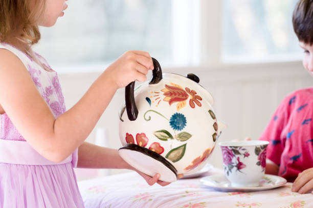 小さな女の子はお茶のパーティー中にお茶を注ぎます - tea party little girls teapot child ストックフォトと画像