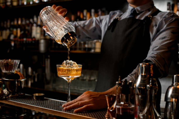 istock Professional bartender in black apron pours drink from shaker into glass. 1224413417