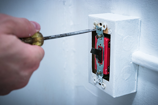Man's hand using screwdriver to replace/repair 20 amp lightswitch on wall