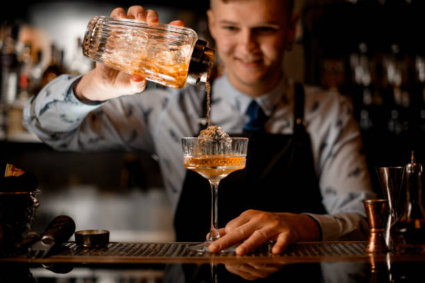istock young smiling bartender professionally pours drink from shaker into glass. 1224416501