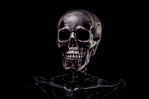 Human skeleton skull in dramatic low key light, corona conid-19 against pitch black background