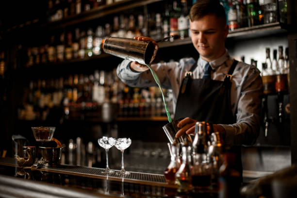 istock young handsome bartender pours cocktail in shaker. Two glasses with ice stand on bar. 1224418700