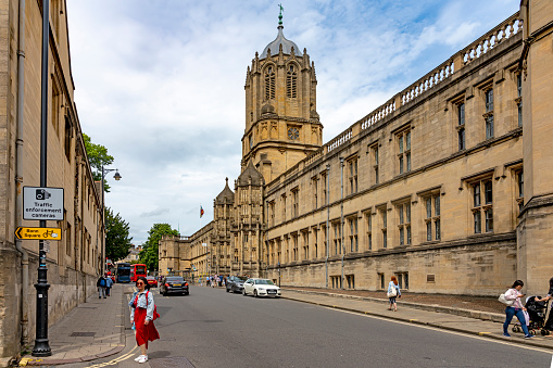 A street in Oxford with an Asian tourist posing for a photograph with the Christchurch Cathedral tower in the background. Oxford , Oxfordshire, England, UK.