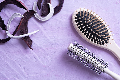 two hair combs and a wooden decoration lie on a textured background and everything is on a pink background