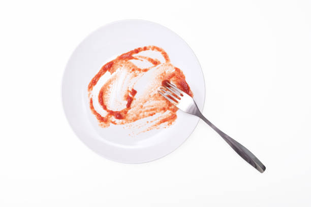 Empty dirty white plate after spaghetti with tomato sause or ketchup on it and a folk on white background.