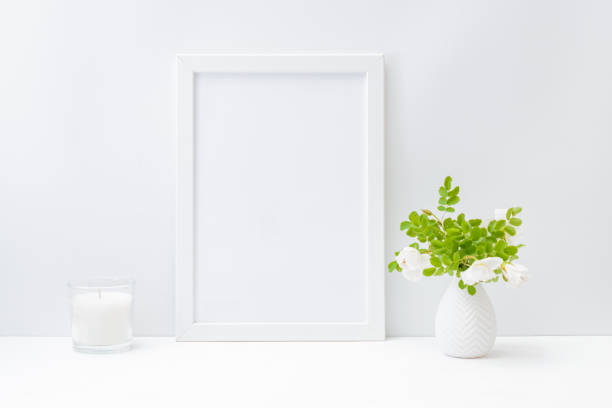 istock Home interior with decor elements. Mockup with a white frame and small flowers and green leaves in a vase on a light background 1224423889