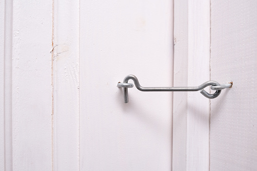 A locked metal door hook on white wooden door, simple device for home house safety and protection.