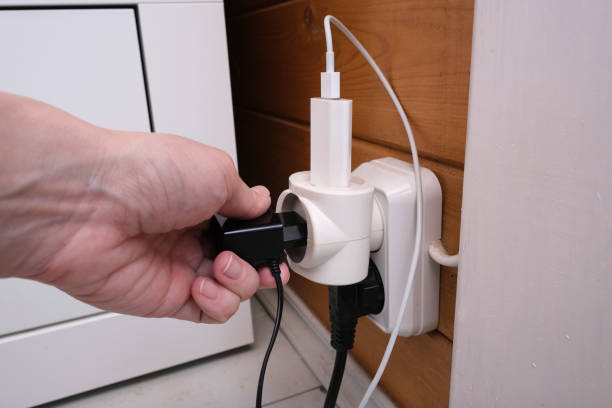 istock Overloaded outlet with an extension and many sockets plugged in, a hand plugging a socket into the outlet, risk of fire and short circuit in a wooden house 1224425589