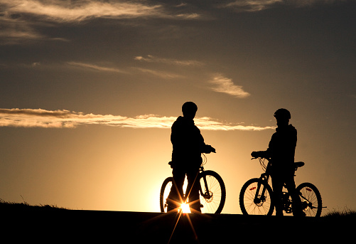An evening silhouette of two cyclists biking down a rural pathway in the prairies. Image taken in rural Alberta near Calgary. Models are unrecognizable.